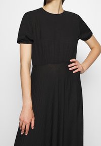 Vestido negro con mangas cortas abullonadas, escote redondo y tela texturizada. Diseño de falda acampanada, acabado suave y corsé ajustado.