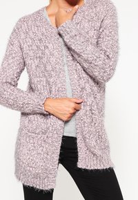 Ljuslila, mjuk stickad kofta med ribbat mönster, öppen fram, och långa ärmar. Har sidofickor och en avslappnad passform.