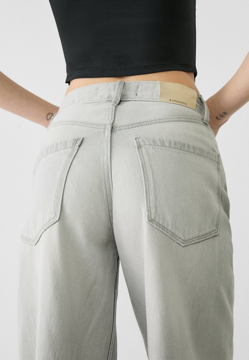 Jeans en denim gris clair à taille haute, dotés d'un tissu texturé, de coutures visibles et de deux poches arrière. Étiquette en cuir sur la ceinture.
