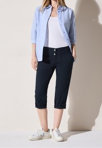 Jasnoniebieska koszula na guziki, biała koszulka na ramiączkach, ciemne krótkie spodnie z dwoma guzikami oraz białe trampki z szarymi akcentami.