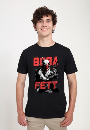 Camiseta negra con un gráfico de un personaje sosteniendo armas, con un texto en rojo negrita que dice "BOBA FETT". El diseño incluye detalles en monocromo.
