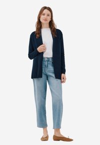 Cardigan navy avec une ouverture à l'avant, manches longues et texture côtelée, associé à un jean droit bleu clair et des chaussures marron.