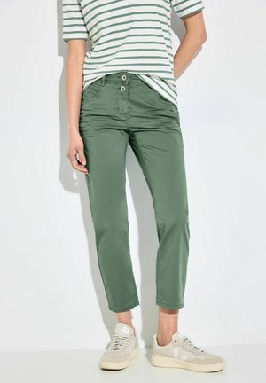 Pantalons en coton mélangé vert avec une coupe fuselée, deux poches avant et deux fermetures à bouton, associés à une chemise rayée et des baskets beiges.