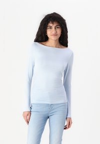 Lys blå langermet topp med båthals, myk tekstur, tett passform og rynkedetalj på siden. Kombinert med lyse jeans.