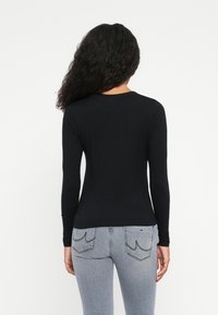 Langärmliges schwarzes Oberteil mit Rundhalsausschnitt, tailliertem Schnitt und weichem Baumwollstoff, kombiniert mit hellen Jeans.