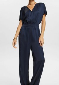Monosuit azul marino con escote en V, mangas cortas y cinturilla elástica. Tejido suave y fluido con un diseño de pierna ancha.
