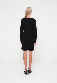 Μαύρο φόρεμα με μακριά μανίκια και φαρδιά τελείωμα. Φτιαγμένο από πλεκτό ύφασμα, έχει απλή και εφαρμοστή σιλουέτα με στρογγυλή λαιμόκοψη.