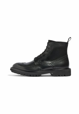 Bota de cuero negro con detalles de brogue, diseño de cordones y una tira de agarre; presenta una suela gruesa y resistente para una tracción mejorada.