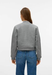 Chaqueta bomber gris con una textura suave, puños acanalados y un cuello. Combinada con jeans de tiro alto azul, vista desde la parte de atrás.