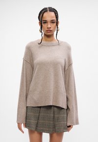 Μπεζ φαρδύ πουλόβερ με ριγωτό λαιμόκοψη, χαμηλούς ώμους και μακριά μανίκια. Συνδυάζεται με καρό μίνι φούστα. Λείο υφή.