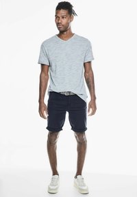 Grijs gestreepte korteblouse v-hals t-shirt gecombineerd met marineblauwe opgerolde shorts. Witte sneakers met lichtgrijze accenten, voorzien van een gestructureerde riem.