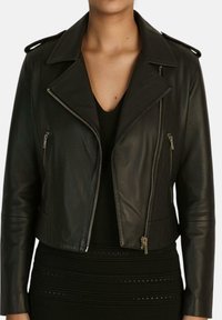 Giubbotto corto in pelle nera con colletto a punte, chiusura con zip frontale e tasche laterali; dotato di accessori in argento e texture liscia.