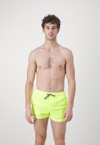 Shorts de baie neon galbeni cu talie elastică, șnur ajustabil și un croi sportiv clasic. Material neted și design minimalist.
