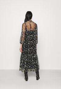 Sort maxikjole med blomsterbroderi, gennemsigtige lange ærmer, lagdelt, rynket nederdel og gennemsigtigt liv. Knappelukning bagpå.