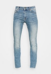 Světle modré džínové kalhoty s přiléhavým střihem, pěti kapsami a mírným vyblednutím podél nohavic. Kovové zapínání na knoflík a zip.