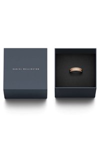Vaaleanpunakultainen sormus tummansinisessä neliömäisessä laatikossa, jonka sisäpuoli on musta. Laatikon kannessa lukee "DANIEL WELLINGTON" kultaisella kirjainnolla.