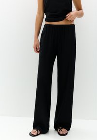 Pantalon noir, ample et à jambes larges, en tissu léger avec une taille élastique et une texture subtile. Associé à un haut noir et des sandales.