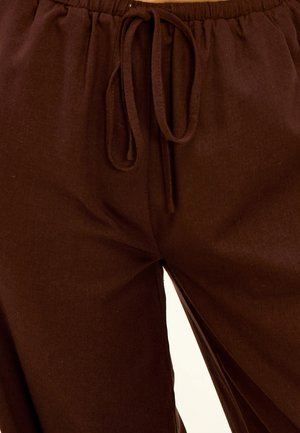 Pantalons marron légers avec une ceinture élastique et un cordon de serrage, avec une texture lisse semblable au lin. Présente des coutures latérales.