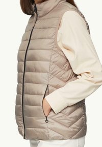 Lekka, beżowa pikowana kamizelka z pionowymi i skośnymi wzorami pikowania, wysokim kołnierzem oraz bocznymi kieszeniami na zamki.