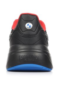 Scarpa sportiva in pelle nera con accenti rossi, caratterizzata da una suola in gomma blu e un logo BMW sul tallone. Texture liscia, forma arrotondata.