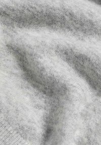 Tessuto a maglia grigio chiaro con una consistenza morbida e soffice, caratterizzato da leggere variazioni di ombreggiatura e motivo sulla superficie.