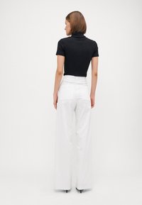 Top negro de manga corta de canalé combinado con pantalones de pierna ancha blancos de talle alto. Los pantalones cuentan con bolsillos traseros y un acabado limpio en el dobladillo.