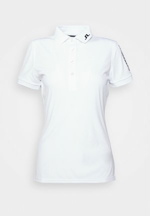 Camisa polo blanca hecha de tejido suave, con una tapeta de botones, un cuello tipo solapa y un logo en la manga. Las mangas cortas están ribeteadas.