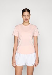 Svijetlopinkana atletčka majica s kratkim rukavima i okruglim izrezom, s malim bijelim Nike logotipom na prsima. Nosiva s bijelim šortsem.