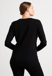 Maglia nera a maniche lunghe con vestibilità morbida, texture soffice, scollatura rotonda e dettagli cuciti sull'orlo. Indossata con leggings neri.