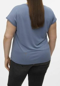 Top blu corto con maniche a sbuffo e una vestibilità rilassata, caratterizzato da una texture morbida e un orlo curvo. Indossato con jeans scuri, che mostrano un design semplice.