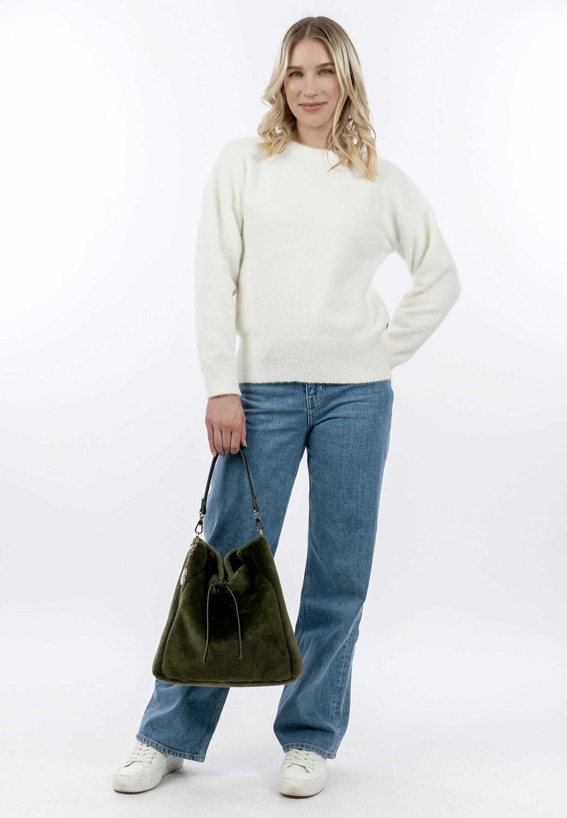 Pull blanc et moelleux à col rond porté avec un jean bleu clair. Le mannequin tient un sac en olive vert à texture douce avec un fermoir à cordon.