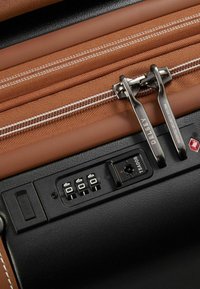 Un tessuto marrone e materiali sintetici neri si combinano in una valigia con doppie cerniere, una serratura TSA e una porta USB per ricaricare i dispositivi.