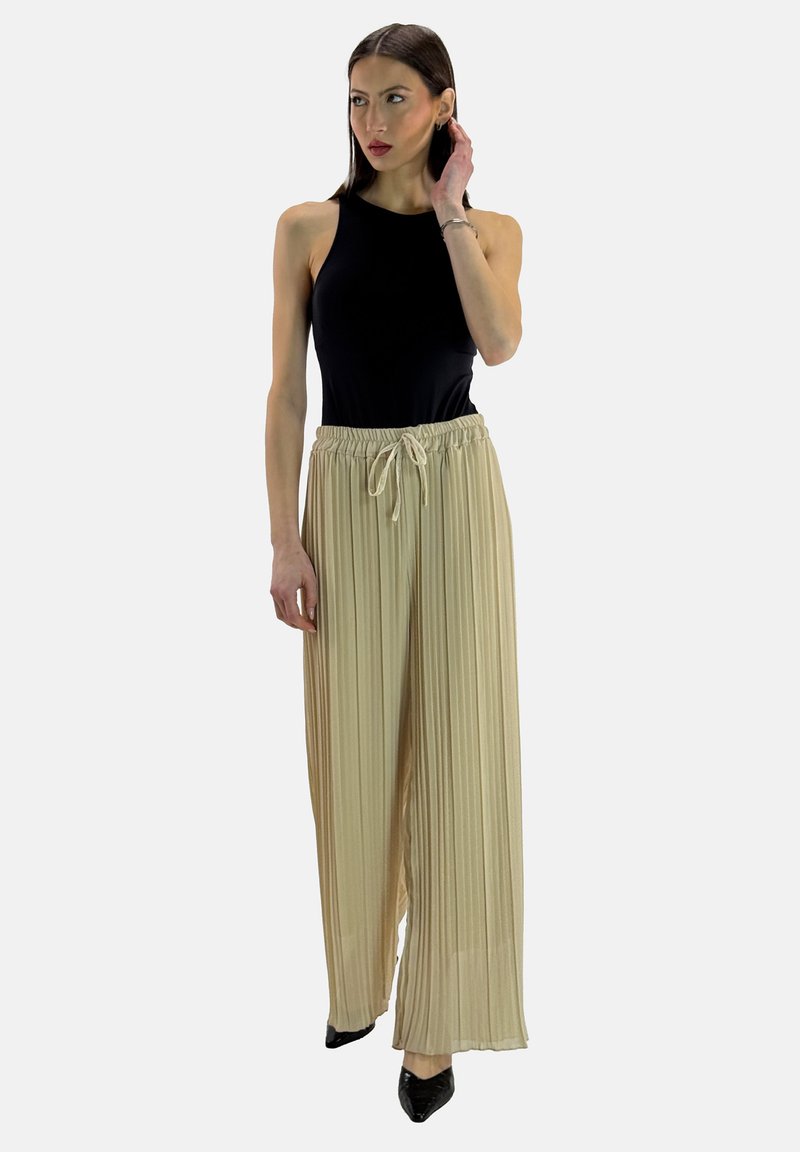 Zwarte mouwloze bodysuit gecombineerd met beige plooibroek, met een elastische tailleband en trekkoord, gedragen met zwarte hakken.
