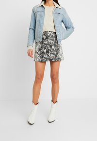 Lichtblauwe spijkerjack met schapenwollen kraag, beige gebreide trui, zwart-wit slangenprint rok en witte cowboylaarzen.