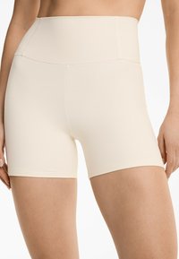 Hoge taille lichtbeige shorts gemaakt van gladde, rekbare stof. Bevat een naadloze tailleband en een aansluitende snit die tot halverwege de dij reikt.