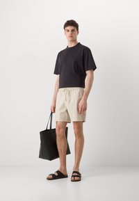Cămașă neagră scurtă, pantaloni scurți bej deschis, sandale negre și o geantă de umăr neagră. Material neted cu talie elastică la pantaloni scurți.