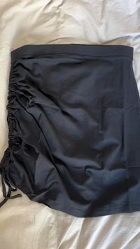 Schwarzer, leichter Stoffrock mit gerafften Seiten und Zugbandsdetails. Glatte Textur, knielanges Design. Keine sichtbaren Muster oder Beschläge.