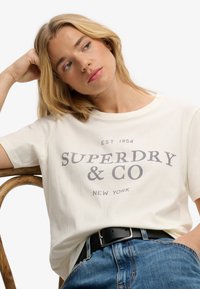 White cotton t-shirt with "SUPERDRY & CO NEW YORK" printed in gray, featuring a relaxed fit, round neckline, and short sleeves.