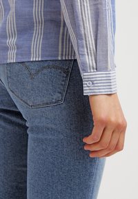 Hellblau-weiß gestreifte Langarmbluse mit geknöpften Manschetten, kombiniert mit dunkelblauen Jeans aus Denim mit einem Design für die Gesäßtasche.