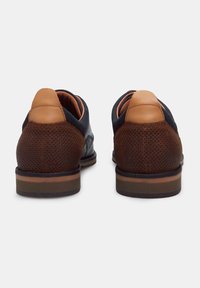 Brown and navy shoes with perforated texture, leather accents, and a flat sole. The heel features a smooth saddle brown panel.