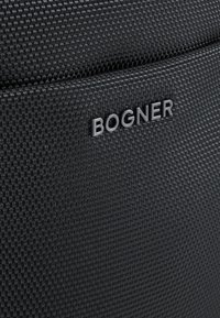 Čierna textilná taška s tkaným vzorom, s vypuklým sivým logom "BOGNER". Materiál vyzerá odolne s jemne textúrovaným povrchom.