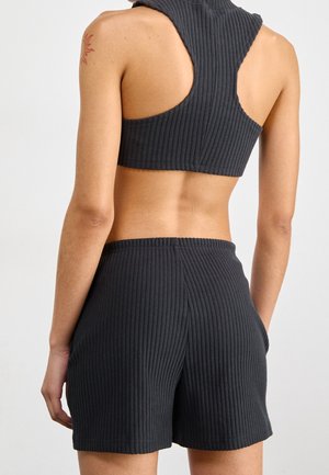 Personne portant un haut court sans manches côtelé gris foncé avec dos nageur, et un short côtelé taille haute assorti, debout de dos face à l'avant.