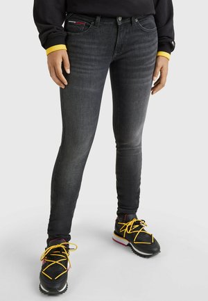Jeans negros ajustados con textura desgastada y costuras sutiles. Llevados con zapatillas negras que tienen cordones amarillos y una suela resistente.