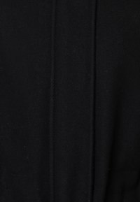 Zwarte wollen stof met een zachte, gestructureerde oppervlakte; heeft subtiele stiknaden die verticaal in het midden lopen voor extra detail.