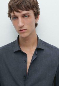 Dark gray button-up shirt made of textured fabric, featuring a pointed collar and an open placket. Plain background.