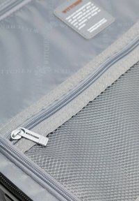 Primer plano del interior de una maleta gris que muestra un bolsillo de malla con cremallera y un tirador metálico con la inscripción "WITTCHEN".