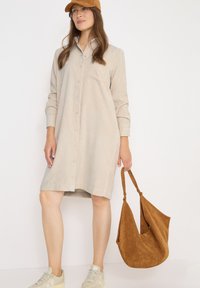 Randig skjortklänning i ljus beige tyg, långärmad, med bröstficka; parat med en brun mockaväska och ljusa sneakers.