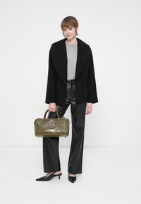 Casaco oversized preto, blusa cinza, calças pretas de imitação de couro de cintura alta, mala verde com detalhe de estrela e sapatos de salto preto com bico pontudo.