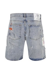 Short en jean bleu clair avec des éclaboussures de peinture, deux poches arrière, passants de ceinture et patches blancs avec des dessins graphiques sur les côtés.