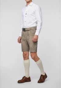 Grå traditionella shorts med broderier, tillsammans med en vit skjorta med knäppning och bruna knappar, bruna skor och krämfärgade knästrumpor.